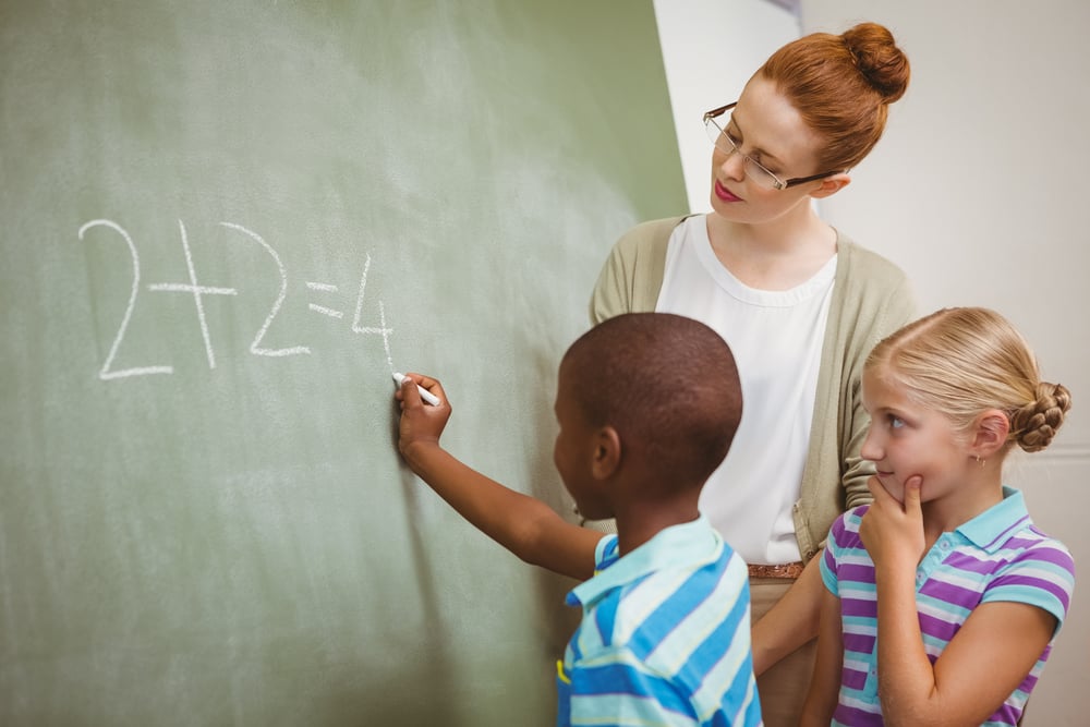 Side view of teacher assisting little boy to write on blackboard in the classroom